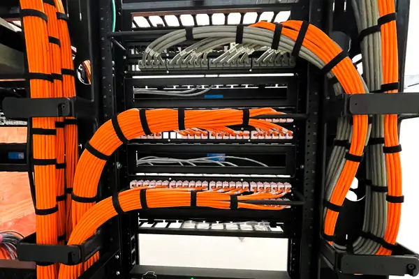 A server rack with neatly organized orange and gray cat six network cables connected to switches. The cables are secured with black cable-ties, showcasing tidy cable management within the rack setup.