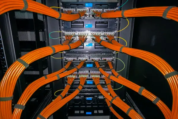 A server rack with multiple orange cat six network cables neatly connected to network switches and patch panels. The setup is organized with labels above each connection, indicating a structured network infrastructure.